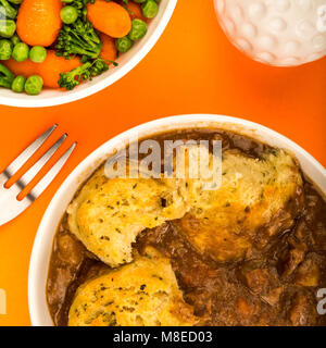 Goulasch de Bœuf britannique traditionnel, avec des boulettes contre un fond orange avec un bol de légumes Banque D'Images