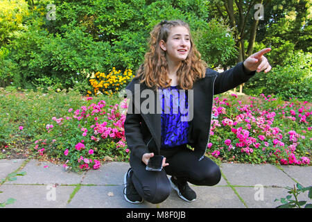 Une jeune fille assise sur un trottoir dans un jardin botanique, pointant vers l'avant Banque D'Images