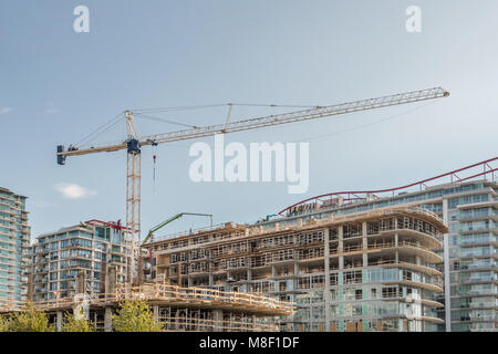 Nouveau bâtiment, construction d'un bâtiment moderne de plusieurs étages avec une grue à tour et autres matériel de construction dans la ville, entre les maisons et arbres Banque D'Images