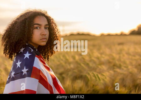 Triste déprimé mixed race African American girl adolescent femme jeune femme dans un champ de blé ou d'orge enveloppés dans USA stars and stripes flag i Banque D'Images