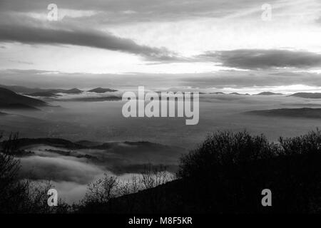 La vallée de l'Ombrie en hiver rempli par la brume au coucher du soleil, avec les collines, les lumières de la ville de Foligno cachés et de beaux tons shot et ombres Banque D'Images