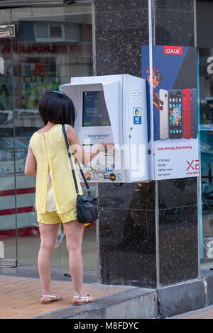 Jeune femme à l'aide porte sur les Top-up kiosk/ machine pour recharger sa carte SIM prépayée et payer ses factures de services Banque D'Images