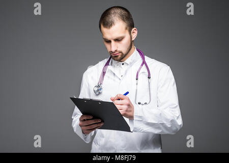 Portrait of smiling barbu tenant le stagiaire avec presse-papiers papier vide. Doc est le port de l'uniforme blanc se dresse sur un fond gris clair Banque D'Images