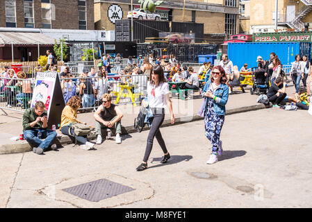 Deux filles hipster marche dans la rue et les personnes bénéficiant de l'été chaud et de manger sur des tables outiside à l'Old Truman Brewery, Ely's Yard, Shor Banque D'Images