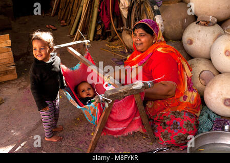 Une indienne en sari rouge robe d'enfants assis à côté des pots de l'eau sur les marchés et la réconforter bébé garçon dans une simple crèche oscillante fabriqués à partir de Banque D'Images