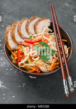 Les nouilles Udon avec des légumes (carottes, poivrons, courgettes, concombre, l'oignon, la coriandre, l'ail), les canards et les graines de sésame. La faire revenir. Selective focus Banque D'Images