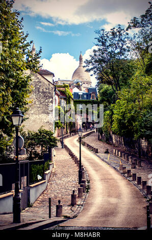 Vue de la route sinueuse s'enfuir entre les trottoirs pavés et vert des arbres sur rue avec l'architecture ancienne à Paris, France Banque D'Images