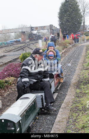 Kidderminster, Royaume-Uni. 17 mars 2018. Météo au Royaume-Uni : alors que le chemin de fer de Severn Valley Railway célèbre un week-end de gala réussi, les amateurs de trains de tous âges connaissent des conditions de blizzard temporaires tout au long de la journée. Malgré des vents forts et amèrement froids, à l'est menant à un refroidissement éolien important, rien n'empêche les fervents (de tous âges!) de profiter d'une promenade en train. Une famille britannique est capturée à l'extérieur dans un blizzard de neige d'hiver, en train miniature! Crédit: Lee Hudson/Alay Live News Banque D'Images