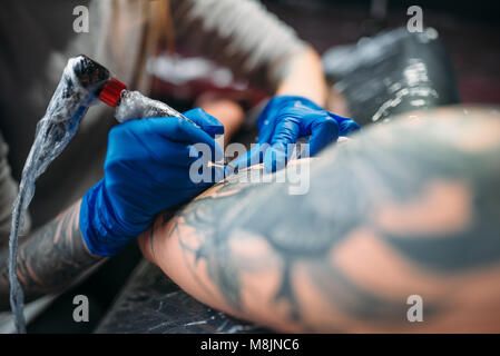 Tatoueur tatouage féminin fait par la machine sur l'épaule masculine. Dans le salon de tatouage professionnel Banque D'Images