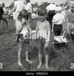 Années 1950, historiques, deux enfants participant à une robe de compétition lors d'une fête en plein air dans un champ portant leurs tenues d'Adam et Eve à court ou costumes. La jeune fille timide est tenant une pomme. Banque D'Images