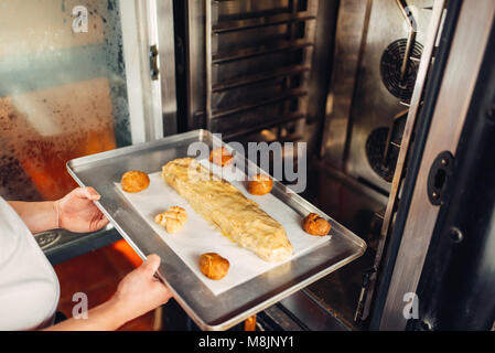 Male chef mains met strudel aux pommes sur une plaque de métal dans le four. Boulangerie, la préparation des desserts sucrés Banque D'Images