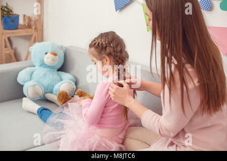 Jeune mère et fille ensemble week-end à la maison assis sur le canapé maman faire hairstile pour fille Banque D'Images