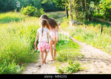 Deux petites sœurs marcher et jouer sur la route en pleine campagne sur un été chaud au coucher du soleil. Cute little girls. Vue arrière Banque D'Images