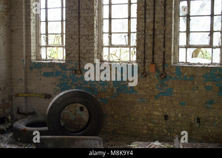 Un vieux bâtiment abandonné avec des fenêtres cassées, de la peinture et de trois pneus utilisés. Banque D'Images