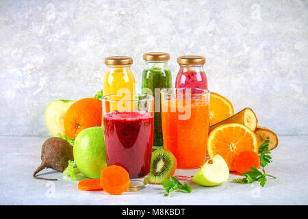 Vert, jaune, violet smoothies en bouteilles de cassis, persil, pommes, kiwi, orange gris sur une table. Smoothies orange et violet dans les verres de betterave et c Banque D'Images