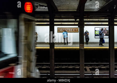 Des hommes se tenant sur la plate-forme de la station de métro 86th Street alors qu'un train arrive sur la plate-forme opposée, Manhattan, New York City Banque D'Images
