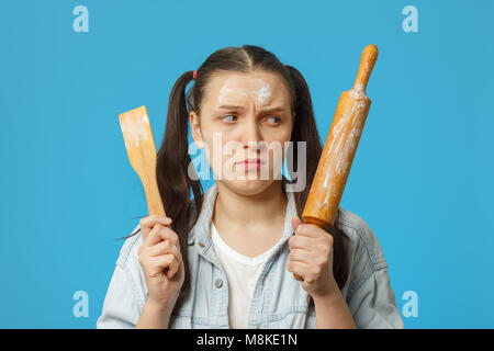 Femme sérieuse avec un rouleau est souillée dans la farine sur fond bleu looking at camera Banque D'Images