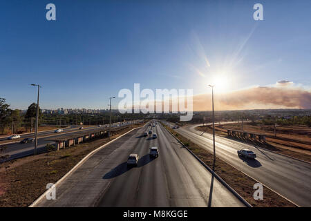 L'autoroute à Brasilia avec les voitures qui transitent, ayant au fond d'un incendie de forêt et la gauche d'une ville. Le ciel était dégagé, laissant la fumée de l'incendie wel Banque D'Images