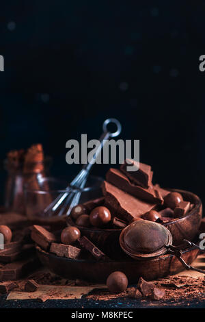 Confiserie maison concept avec le chocolat fondu dans une tasse en verre vitrage avec un fouet. Morceaux de chocolat éparpillés, le cacao en poudre et la cannelle sur un b Banque D'Images