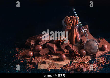 En-tête avec la cannelle dans un bocal en verre, de poudre de cacao et des morceaux épars de brisures de chocolat sur un fond sombre avec copie espace. Je ingrédients dessert Banque D'Images