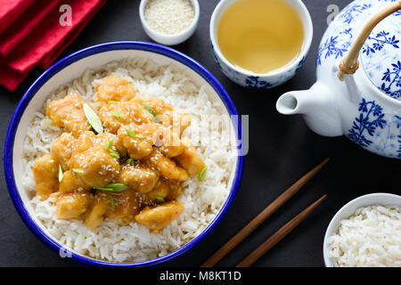 Sésame asiatique ou du poulet teriyaki avec du riz dans un bol, du thé vert et baguettes sur fond sombre. Vue d'en haut Banque D'Images