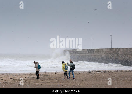 Ramsgate, Kent, UK 18 Mars, 2018. Trois jeunes femmes marcher sur plage de Ramsgate lors d'une tempête de neige alors qu'une grosse vague s'écrase dans le port arm. Sue Holness Crédit : Sue Holness/Alamy Live News Banque D'Images