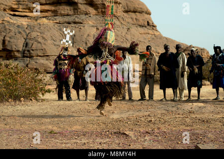 Un groupe de danseurs masqués Dogon regarder un homme portant une coiffe imposante effectuer sa part dans une danse traditionnelle. Pays dogon, Mali, Afrique de l'Ouest. Banque D'Images