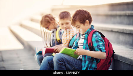 Les enfants avec des sacs à dos assis sur l'escalier près de l'école Banque D'Images