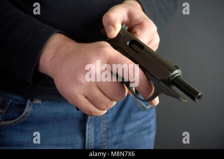 Close up de la main de l'homme, l'homme d'armes à feu de rechargement et munitions chargement de tenir son pistolet sur fond sombre. Banque D'Images