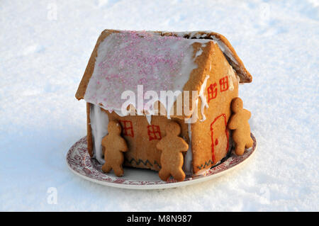 Une maison en pain d'épices fait maison avec du gingembre les hommes sur une plaque assis dans la neige. Banque D'Images