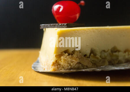 Morceau de gâteau au fromage avec cerise sur fond sombre et de tables en bois Banque D'Images