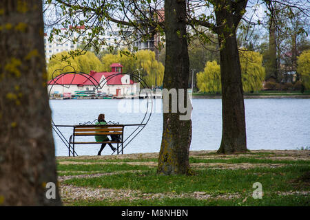 Femme seule assise seule sur un banc dans un pack près du lac Banque D'Images