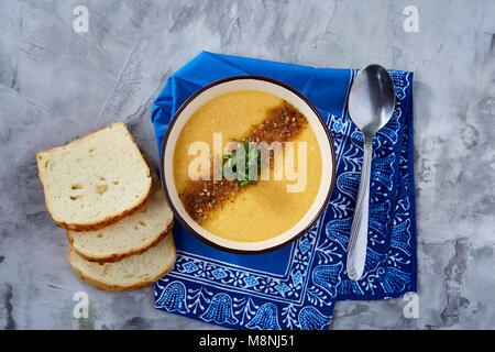 Bol en porcelaine violet de soupe de potiron crémeuse garnie d'aneth, servi avec des tranches de pain grillé sur bure sur serviette fond texturé blanc, Banque D'Images