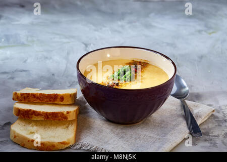 Bol en porcelaine violet de soupe de potiron crémeuse garnie d'aneth, servi avec des tranches de pain grillé sur bure sur serviette fond texturé blanc, Banque D'Images