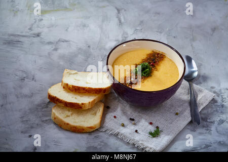 Bol en porcelaine violet de soupe de potiron crémeuse garnie d'aneth, servi avec des tranches de pain grillé sur bure sur serviette fond texturé blanc, Banque D'Images