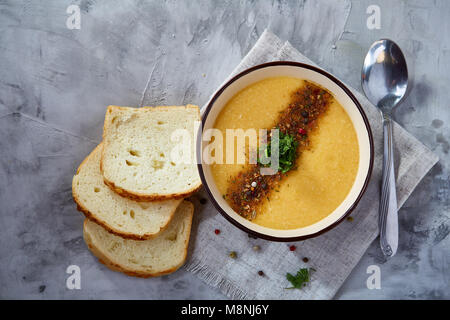 Bol en porcelaine violet de soupe de potiron crémeuse garnie d'aneth, servi avec des tranches de pain grillé sur bure sur serviette fond texturé blanc, Banque D'Images