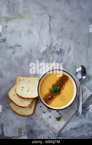 Bol en porcelaine violet de soupe de potiron crémeuse garnie d'aneth, servi avec des tranches de pain grillé sur bure sur serviette fond texturé blanc, Banque D'Images