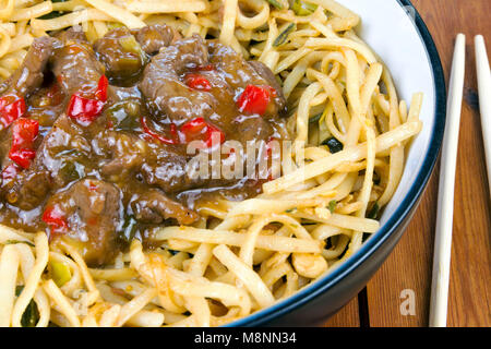 Boeuf épicé avec Sichuan nouilles frites dans un plat close up avec des baguettes sur une table en bois Banque D'Images