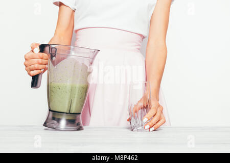Jeune femme mince dans une jupe rose verse un smoothie vert d'une banane et d'épinards dans un verre Banque D'Images