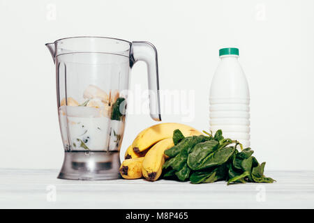 Des smoothies dans un processeur de nourriture d'une banane, les épinards et le lait sur un fond blanc Banque D'Images