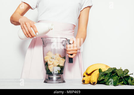 Jeune femme dans la cuisine se déverse le kéfir pour smoothies de la banane et de l'épinard, close-up Banque D'Images