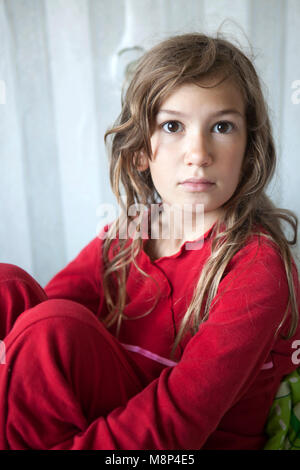 Portrait de jeune fille endormie 11 ans en pyjama rouge assis sur le lit Banque D'Images