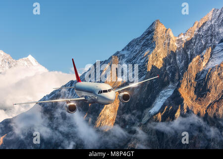 C'est avion survolant les nuages bas contre des montagnes avec des sommets enneigés en plein jour. Paysage. Avion de passagers, ciel nuageux, rochers, neige. Passager Banque D'Images