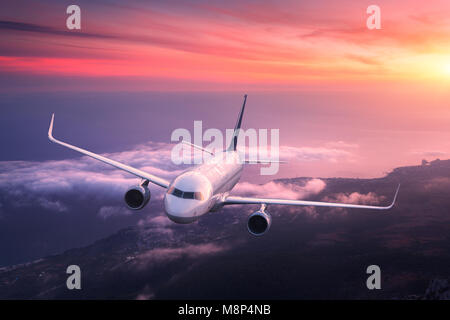 Avion de passagers. Paysage avec Big White est un avion volant dans le ciel rouge sur les nuages et la mer au coucher de soleil colorés. Avion de passagers est landi Banque D'Images