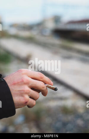 Libre d'un jeune homme de race blanche à l'extérieur fumer une cigarette roulée à la main ou une co Banque D'Images