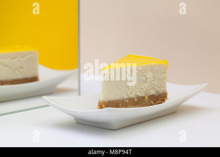 Un morceau de gâteau au fromage au citron sur une plaque blanche. Reflet dans le miroir. Banque D'Images