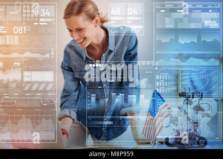 Smiling woman looking at her laptop while un robot assis à côté d'elle Banque D'Images