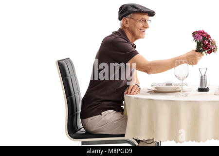 Homme mature avec un bouquet de fleurs assis à une table de restaurant isolé sur fond blanc Banque D'Images