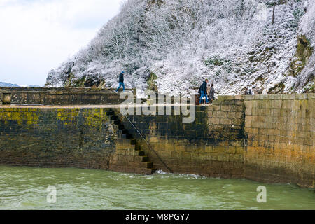 18/03/2018 Charlestown, Cornwall, UK, Editorial : inconnu des membres du public en marchant le long du mur du port de Charlestown avec falaises couvertes de neige Banque D'Images