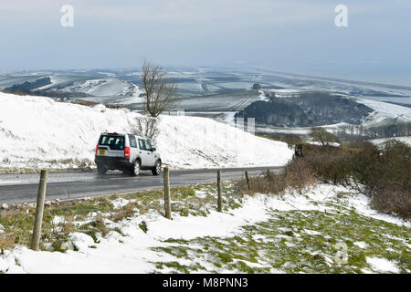 Abbotsbury, Dorset, UK. 19 mars 2018. Météo britannique. Une voiture conduit par un transport de la neige qui borde la route côtière B3157 sur la colline près de Abbotsbury Abbotsbury dans Dorset sur une froide journée glaciale. Dans la distance est l'emblème de la Chapelle Sainte Catherine. Crédit photo : Graham Hunt/Alamy Live News. Banque D'Images